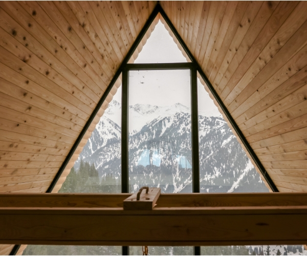 Résidence secondaire en France - Design d'Espaces - Vue sur montagne enneigé depuis l'intérieur d'un châlet par baie vitrée triangulaire, avec plafond en lattes de bois