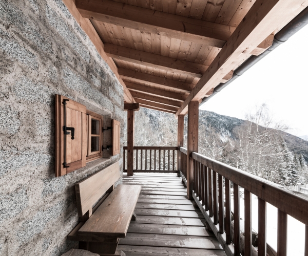 Résidence secondaire en France - Design d'Espaces - Vue sur un paysage enneigé depuis le balcon d'un chalet à la montagne, ou l'on aperçoit une partie de de la façade avec un banc le long du mur